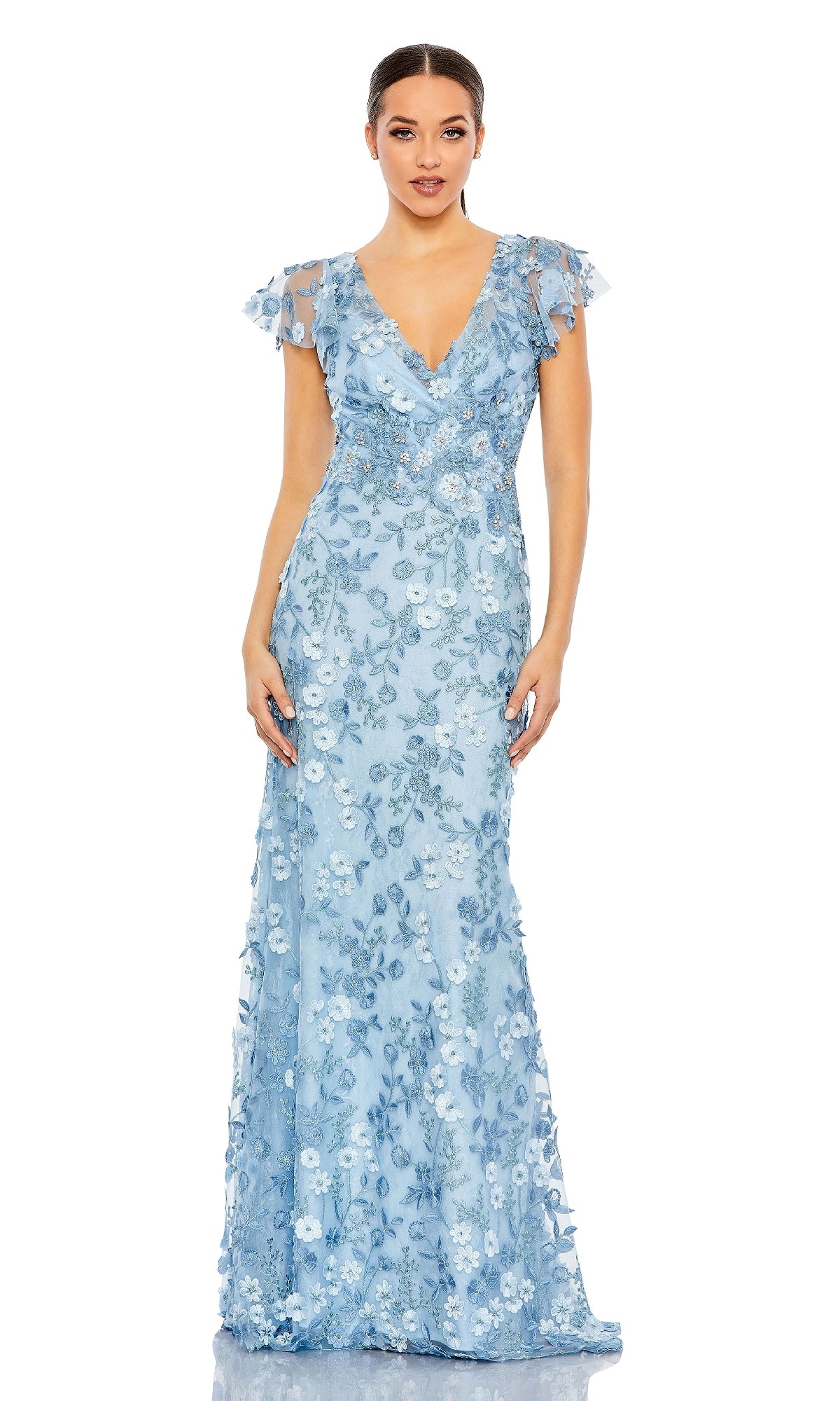 A woman stands against a plain white background wearing the Mac Duggal 68192 Long Beaded Formal Dress, featuring floral embroidery, short flutter sleeves, and a deep V-neckline in light blue.